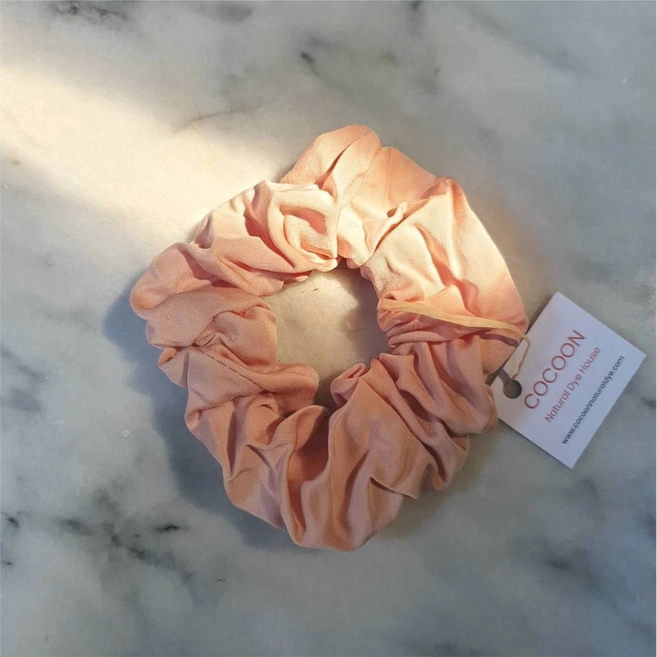 Pink bamboo silk scrunchie pictured on a marble background with a streak of sunshine dashed across the scrunchie