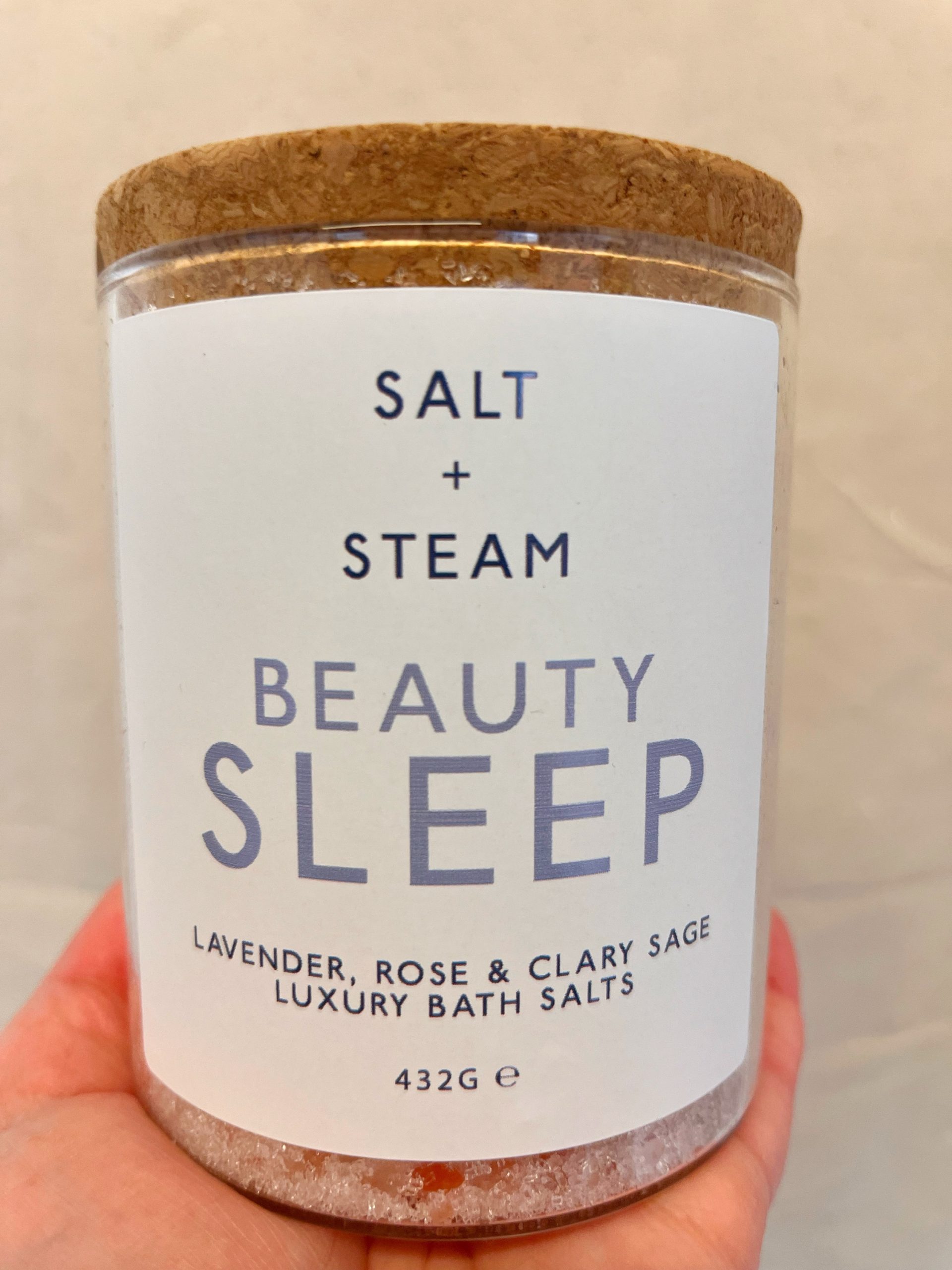 Beauty Sleep Bath Salts by Salt + Steam against a neutral background. The bath salts are in a clear glass jar with a real cork lid.