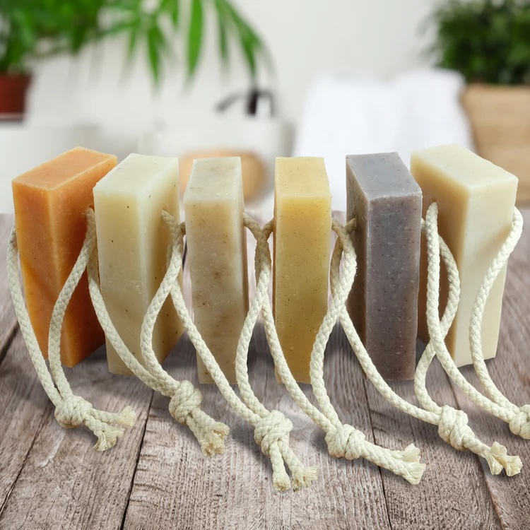 6 bars of soap on a rope in a row. They are stood on brown wooden flooring with the white rope cords visible.